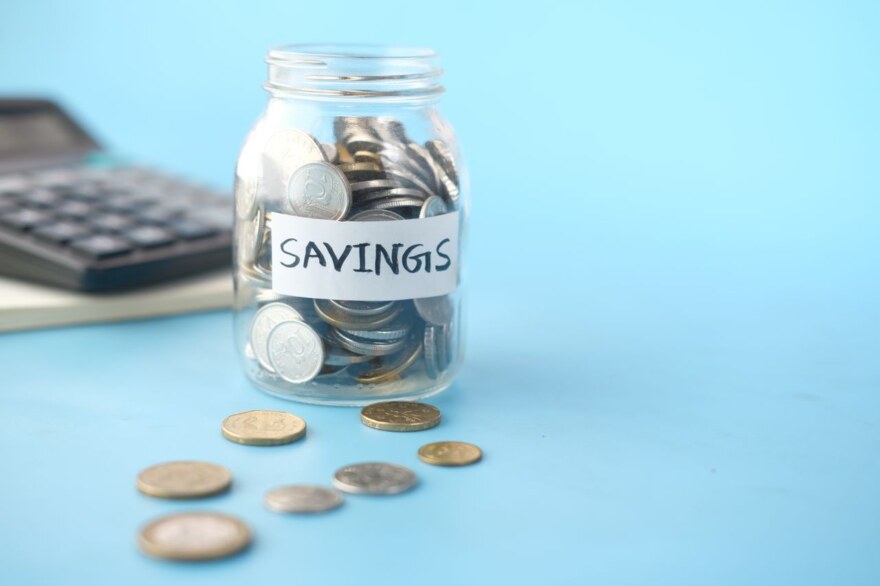 Glasburk med mynt märkt Savings bredvid en miniräknare på blå bakgrund
